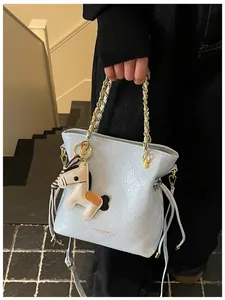 Detail of light blue quilted bucket bag with gold chain and leather horse charm accessory