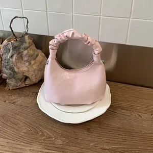 Close-up of pink crescent handbag featuring unique ruched handle and lychee texture