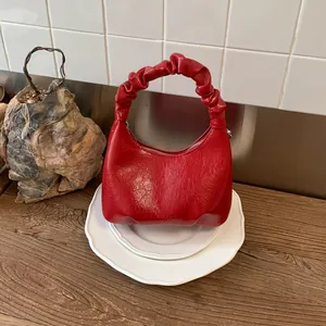 Detail of red ruched leather handbag showing textured surface and handle on ceramic plate