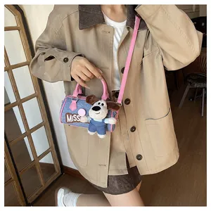Mini denim Boston bag with pink trim and cute plush puppy charm worn by a model