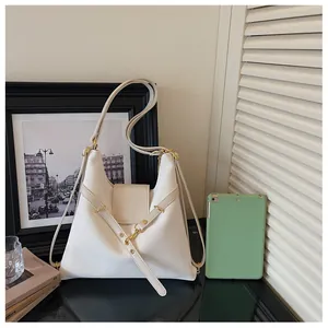 Detail van de crème lederen tote bag met goudkleurige gespen en reliëflogo op de flap