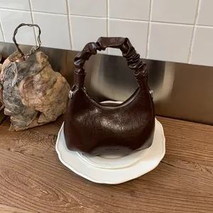 Detailed view of dark brown glossy leather handbag with ruched handle on white plates