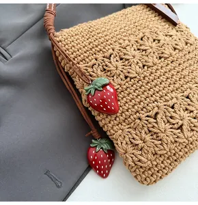 Gros plan d'un sac en paille tissée avec breloques fraises rouges et bandoulière brune