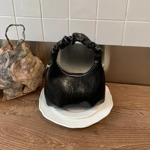 Detail of black pleated shoulder bag with crescent shape and vintage wax leather texture