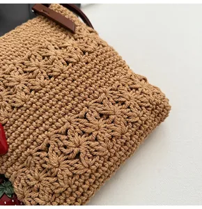 Gros plan du sac en crochet kaki avec bandoulière en cuir et breloque fraise