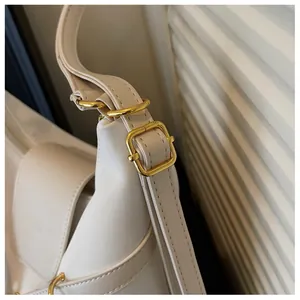 Detail van de verstelbare riem met gouden gesp op een crème kunstlederen tas