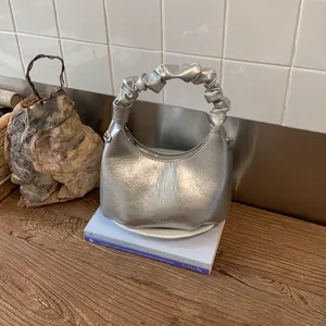 Detail of silver metallic pleated hobo bag with scrunchie handle on wooden surface