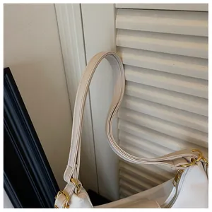Detail van witte waxleren tas met gouden metalen beslag en stiksels op de schouderband