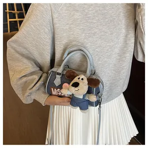 Close-up of denim Boston bag with leather handles and cute plush dog charm detail