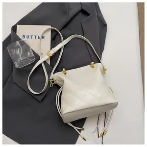 Detail of white quilted drawstring bucket bag with leather strap on grey fabric