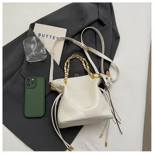 Close-up of beige quilted bucket bag with chain handle, drawstring, and dog charm