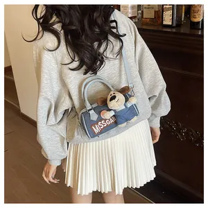 Detail of denim Boston bag featuring a plush puppy pendant and brown leather trim
