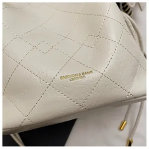 Close-up of beige quilted leather bucket bag featuring gold fashion lettering and drawstring
