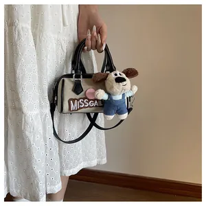 Detail view of cream Boston bag with leather handles and cute plush puppy charm