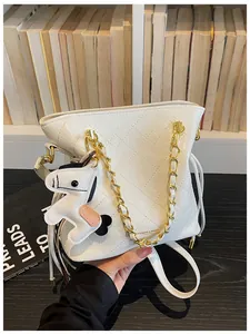 Detail of white quilted bucket bag with gold chain strap and horse charm on shelf