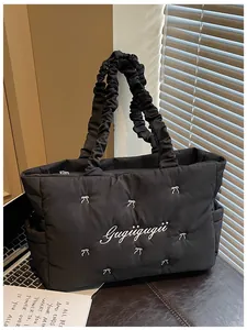 Detail of black quilted nylon tote featuring white bow embroidery and ruffled handle