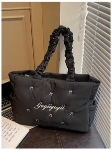 Detail of black quilted nylon tote with white bow embroidery and cloud-shaped strap