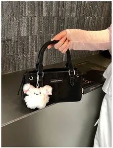 Detail of black textured bucket bag with fluffy bear charm and gold brand plaque
