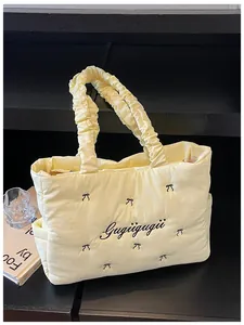 Close-up of yellow quilted nylon tote bag with bow embroidery and ruffled handle detail