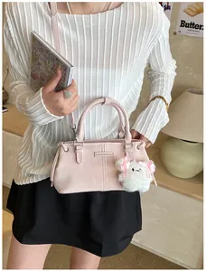 Close-up of pink leather bucket bag with a white plush poodle charm in a cozy indoor setting