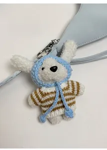 Détail d'une peluche blanche douce avec une cape bleue à capuche et un pull à rayures