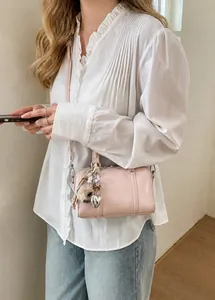 Detail of pink cylinder crossbody bag featuring metal heart charm and leather texture