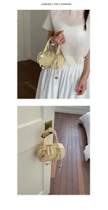 Detail of light yellow Boston bag with heart charm and beaded chain on a white door