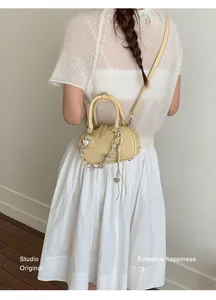 Detailed view of yellow barrel crossbody bag with heart charms and woven pendant strap