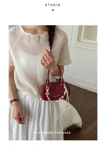 Detail of dark red patent leather handbag with heart charm and woven strap detail