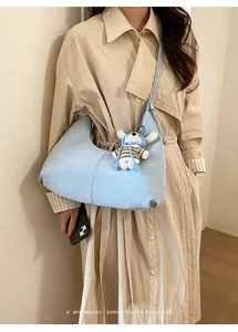 Détail du sac hobo plissé bleu clair avec breloque d'ours sur un trench-coat minimaliste