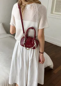 Detailed view of a dark red glossy leather mini bag with a beaded decorative charm