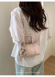 Detail of pink Boston bag with fuzzy pom-pom and heart charms on a female model