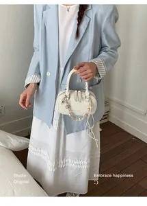Detail of white leather shoulder bag with beaded charm and double zipper closure