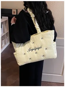 Detail of light yellow quilted tote bag featuring black bow embroidery and ruched strap
