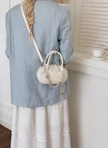 Detail of cream mini leather bag with beaded charm and Pantone lettering strap