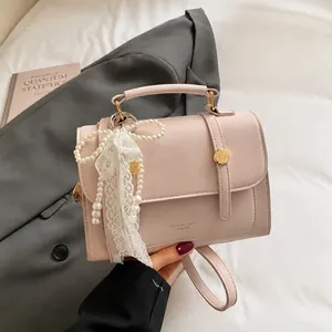 Detail of light pink PU leather handbag with gold clasp and pearl lace charm on grey suit