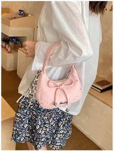 Roze halvemaanvormige tas met zilveren sterren, strik en kattenhanger aan een model