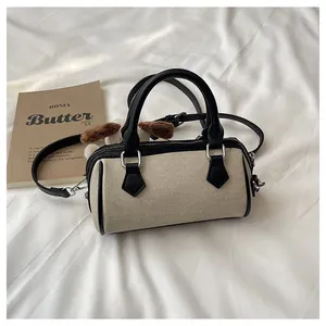 Close-up of beige Boston bag with black leather trim, long strap, and cute puppy charm