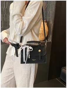 Detail of black leather crossbody bag with gold hardware, lace ribbon and pearl charm