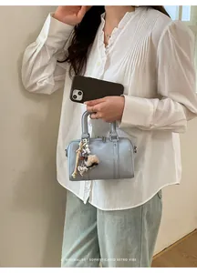 Detail of light blue patent leather boston bag with charms held by a model