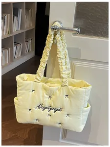 Detail of yellow quilted tote bag featuring black bow embroidery and ruched cloud handle