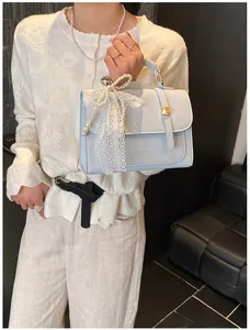 Detail of light blue square handbag with pearl charms and white lace bow decoration