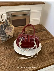 Detail of burgundy leather mini bag with contrast stitching and beaded rope charm
