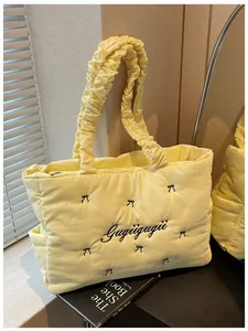 Detail of light yellow quilted nylon tote bag with black bows and ruffled shoulder strap