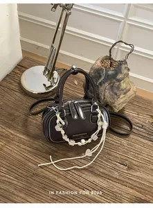Detailed view of dark brown leather crossbody bag with white stitching and bead charm