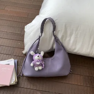 Sac dumpling plissé violet avec bandoulière tressée et breloque lapin sur un oreiller