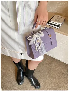 Detail of purple matte leather handbag featuring pearl bow and delicate lace ribbons
