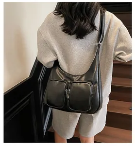 Detail of a black hobo shoulder bag with double pockets worn by a model in a minimal setting