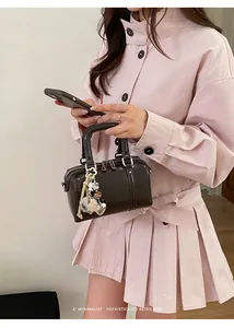 Detail of dark brown mini Boston bag with heart charm and plush ball accessory