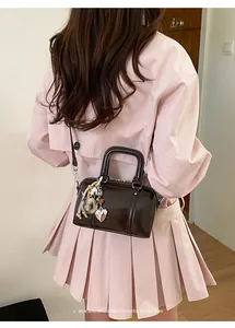 Detail of dark brown patent leather Boston bag with silver heart charm and plush pompom